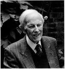 An elderly white man in a chequered jacket, tie and pullover. He is smiling in a garden.