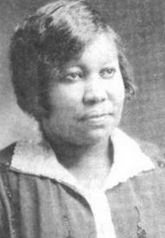 A Black woman with hair cut into a side-parted bob, wearing a white collared blouse and a darker cardigan, in an oval frame