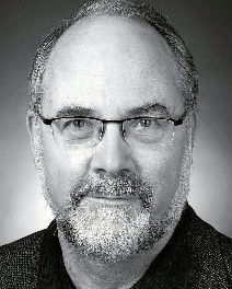 Bespectacled man with neat, short, greying hair and beard, and receding hairline.