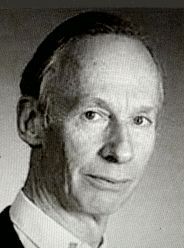 Publicity shot of a slim-faced, clean-shaven man with receding, short hair, aged about 50