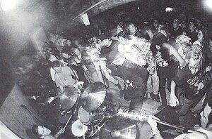 A Fishwife show from 1992 picturing Chris Prescott (on drums, far left), Ryan Foxe (with microphone, black shirt, and cap in front of drum set), Gar Wood (with guitar, left of drum set), and Matt Ohlin (with bass guitar, just visible in lower right corner).