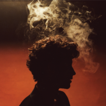 Dark silhouette of Shawn Mendes on an orange background with smoke above his head