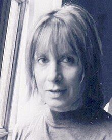 A woman in a turtle-necked shirt with a pageboy hairstyle standing in front of a window