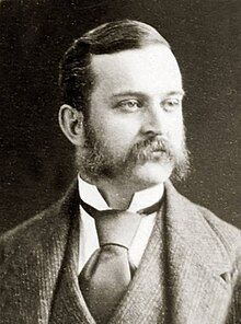 Photograph of a man in middle age, with extravagant sideburns, wearing formal Victorian civilian dress.