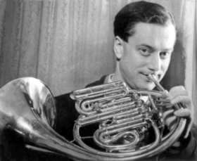 Young white man, clean-shaven, with groomed dark hair, holding French horn