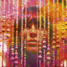 A woman standing stares upwards behind a series of hanging beads; the centre of her face is visible. The image is overlaid with alternating shades of red, pink, purple, orange and yellow.