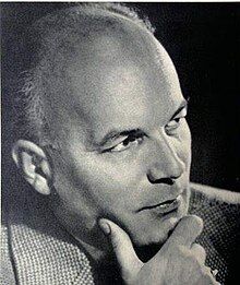 Three-quarter-profile, black and white publicity shot of clean-shaven man with receding hair, with his chin resting on his hand.