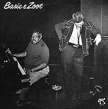 A grayscale photo of Count Basie sitting at a piano and Zoot Sims standing next to him, smoking, with his head tilted down. At the top left corner there is the "Basie & Zoot" text.