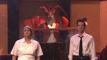 A person in a lobster costume standing in a lobster tank behind two waiters