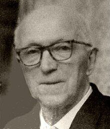 Formal portrait of an elderly, clean-shaven man with receding white hair, and spectacles