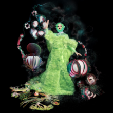 The artist in a long, bright green gown that resembles grass, surrounded by floating plants on a black background.