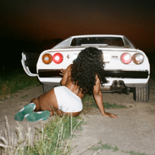 Cover art for "Snooze": SZA in white shorts, sitting on the ground behind a white Ferrari car