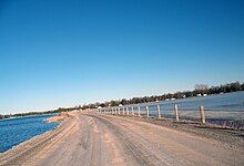 "a dirt road crosses the centre of a lake on a clear day."