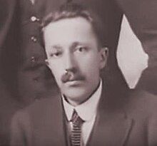 Black and white photograph of a young man with a moustache, dressed in a jacket and tie