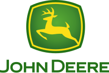 A green, rounded square with a yellow jagged outlines on the four sides of the square near the outside of its green border can be seen. In the middle of the yellow outline, a biological entity drawn outlined in yellow can be seen in a leaping position. This animal is commonly referred to as a deer. Underneath the deer and the green box, the words in small caps, 'JOHN DEERE' can be read.