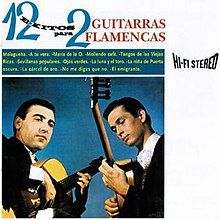 Two men in black suits playing flamenco guitars in front of a blue background