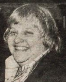 A smiling white woman with grey hair cut in a blunt bowl-style cut