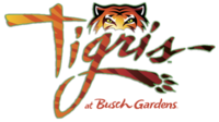 A script text "Tigris" in an orange gradient, trimmed in green, with sublimated tiger stripes. The tail of the "g" curls around and ends in a paw print. An illustration of the top half of the head of a tiger, featuring its eyes, sits atop the script. The words "at Busch Gardens" are in red, tucked into the lower right corner.