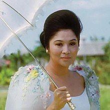 An image of Imelda Marcos, former First Lady of the Philippines, holding an umbrella while wearing a dress.