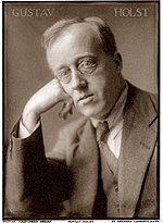 A sepia-toned white man in glasses and a suit looks at the viewer.