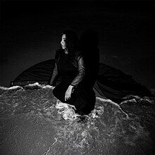 A black-and-white photo of Aftab kneeling in shallow beach water.