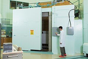 A man using a control panel to open a large concrete door into a small room constructed of thick concrete walls attached to the reactor. This room is for utilizing a neutron beam for neutron radiography.