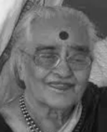 An older South Asian woman wearing glasses, beads, a sari and a large bindi.